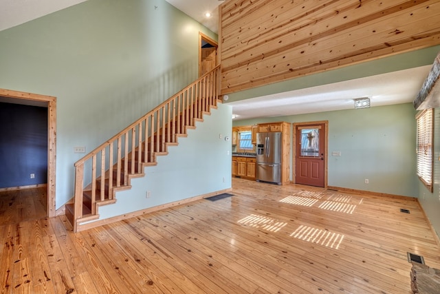 interior space featuring visible vents, light wood-style floors, a high ceiling, baseboards, and stairs