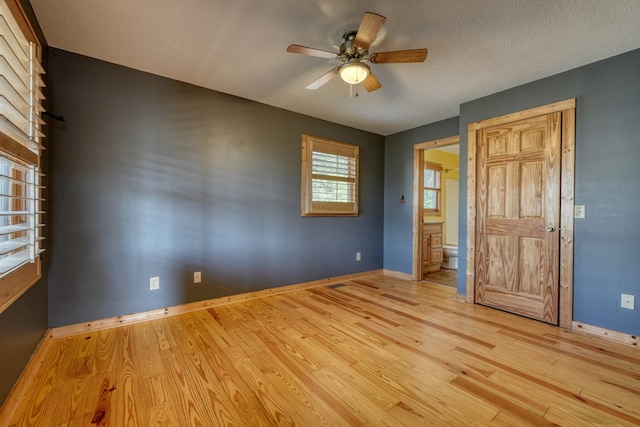 unfurnished bedroom with ensuite bath, light wood-style flooring, baseboards, and a textured ceiling