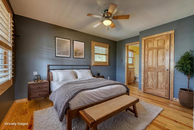 bedroom featuring baseboards, ceiling fan, ensuite bathroom, and light wood finished floors