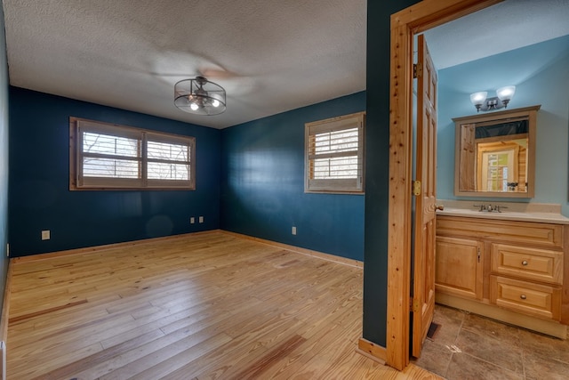 unfurnished room featuring baseboards, plenty of natural light, a textured ceiling, and light wood finished floors