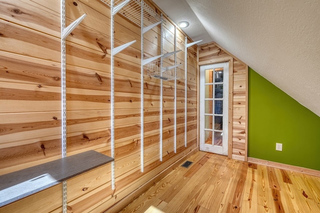 additional living space with wooden walls, visible vents, lofted ceiling, hardwood / wood-style floors, and a textured ceiling