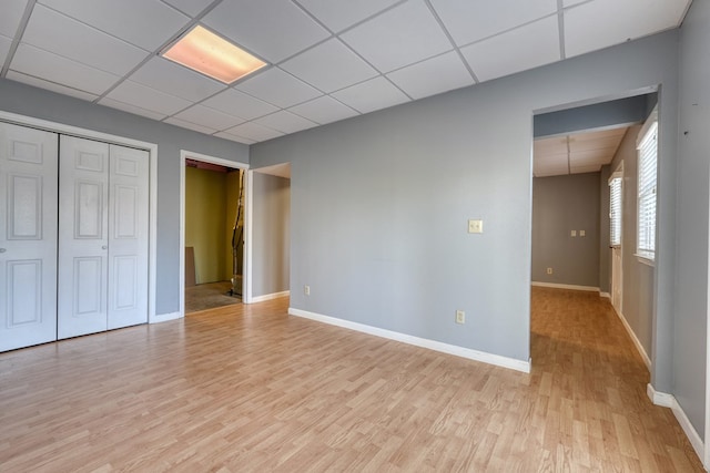 interior space featuring a drop ceiling, baseboards, a closet, and light wood finished floors