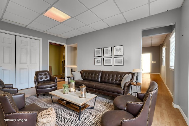 living room featuring a drop ceiling, baseboards, and wood finished floors