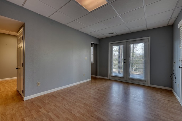 empty room featuring french doors, a paneled ceiling, baseboards, and light wood-style flooring