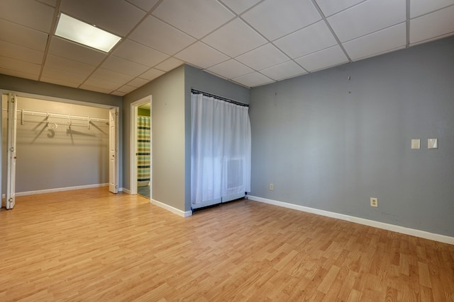 unfurnished bedroom with light wood finished floors, a drop ceiling, a closet, and baseboards