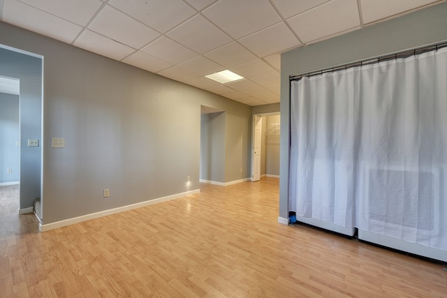 spare room with baseboards, a paneled ceiling, and light wood-style flooring