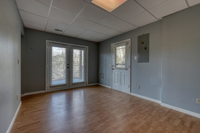 unfurnished room featuring wood finished floors, electric panel, a paneled ceiling, and french doors