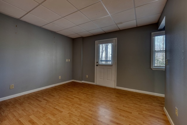 unfurnished room with baseboards, a paneled ceiling, a healthy amount of sunlight, and light wood finished floors