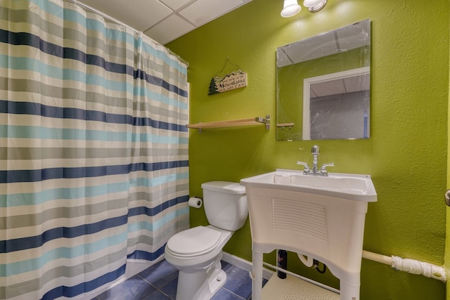 full bath featuring a shower with shower curtain, a drop ceiling, tile patterned floors, toilet, and a textured wall