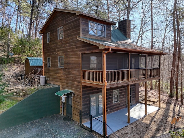 view of side of home with a sunroom, a chimney, and a patio area