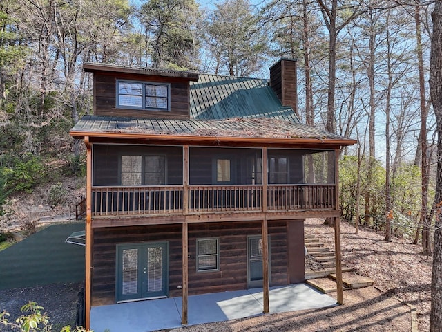 rear view of house featuring french doors, a chimney, metal roof, a sunroom, and a patio area