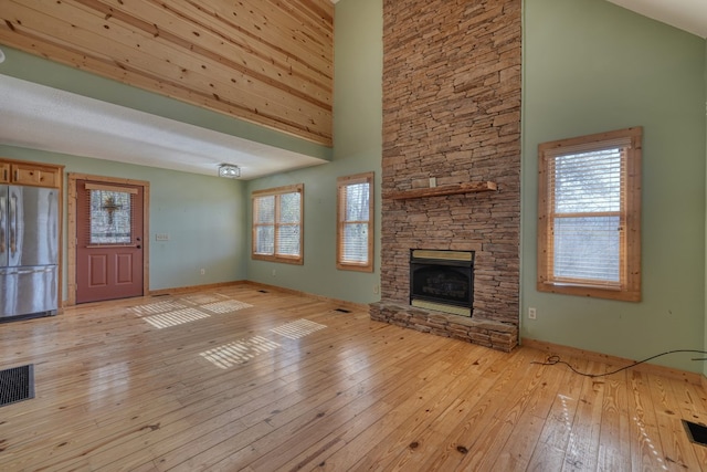 unfurnished living room featuring a high ceiling, a fireplace, visible vents, and light wood finished floors