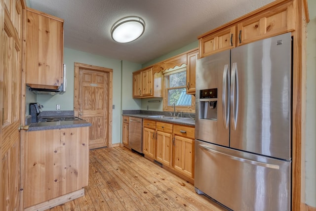 kitchen featuring a sink, stainless steel appliances, light wood-style floors, a textured ceiling, and dark countertops