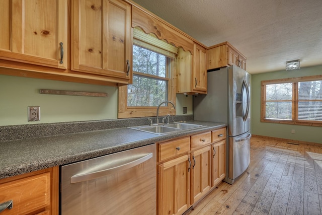 kitchen featuring light wood finished floors, a sink, stainless steel appliances, a textured ceiling, and dark countertops