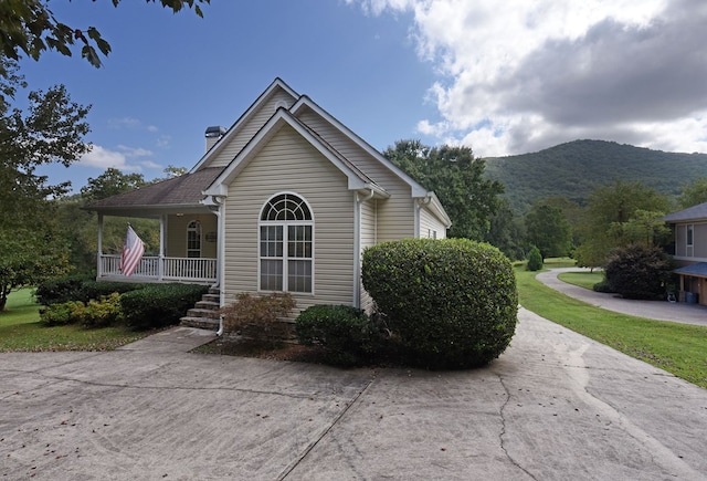 view of side of property with a mountain view, a lawn, a porch, and a chimney