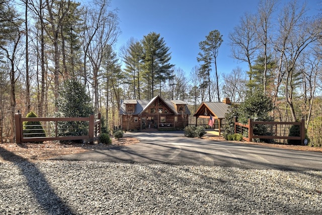 view of front facade with gravel driveway, a chimney, fence, and metal roof