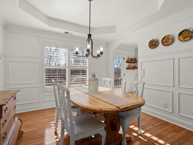 dining space featuring an inviting chandelier, a tray ceiling, light hardwood / wood-style flooring, and ornamental molding