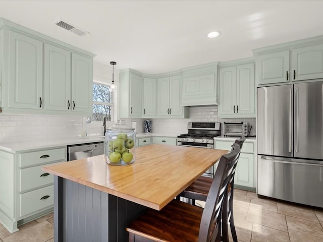 kitchen featuring appliances with stainless steel finishes, decorative light fixtures, tasteful backsplash, a center island, and custom range hood