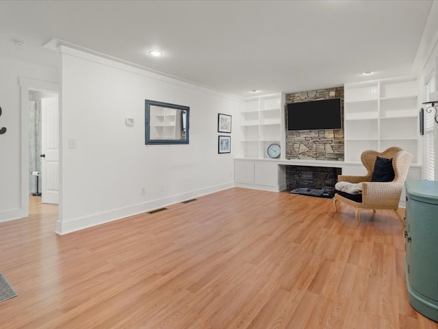 unfurnished living room featuring crown molding, a stone fireplace, light hardwood / wood-style floors, and built in shelves