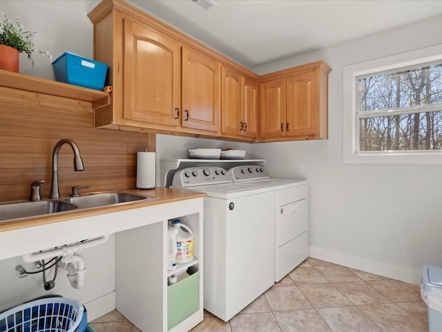 clothes washing area with sink, light tile patterned floors, washer and clothes dryer, and cabinets