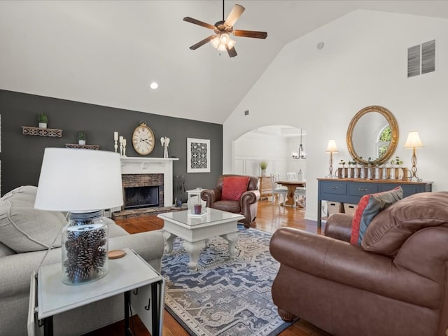 living room with hardwood / wood-style flooring, a stone fireplace, high vaulted ceiling, and ceiling fan