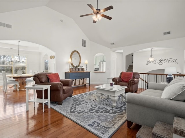 living room with hardwood / wood-style floors, ceiling fan with notable chandelier, and high vaulted ceiling