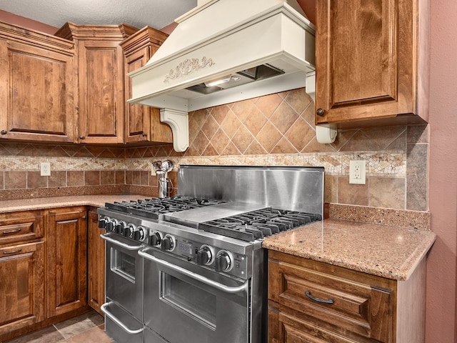 kitchen featuring high end range, premium range hood, a textured ceiling, tasteful backsplash, and light stone counters