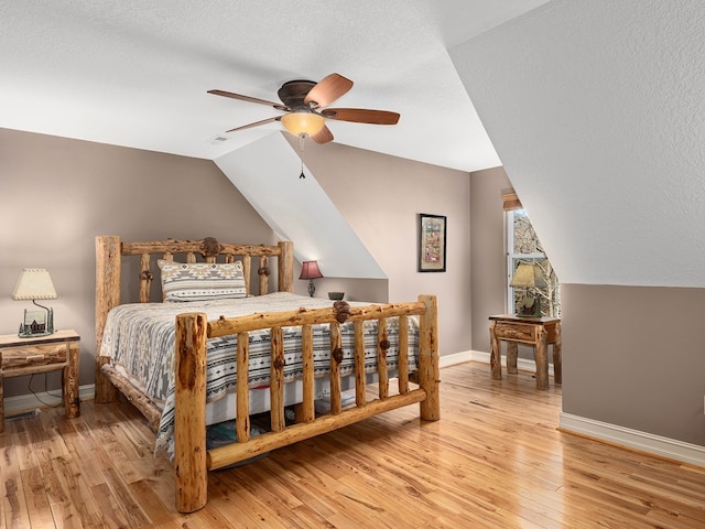 bedroom with a textured ceiling, light wood-type flooring, vaulted ceiling, and ceiling fan