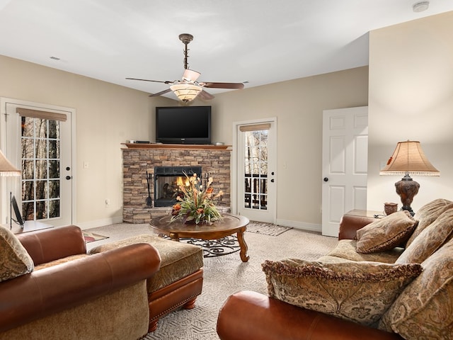 carpeted living room with a stone fireplace and ceiling fan