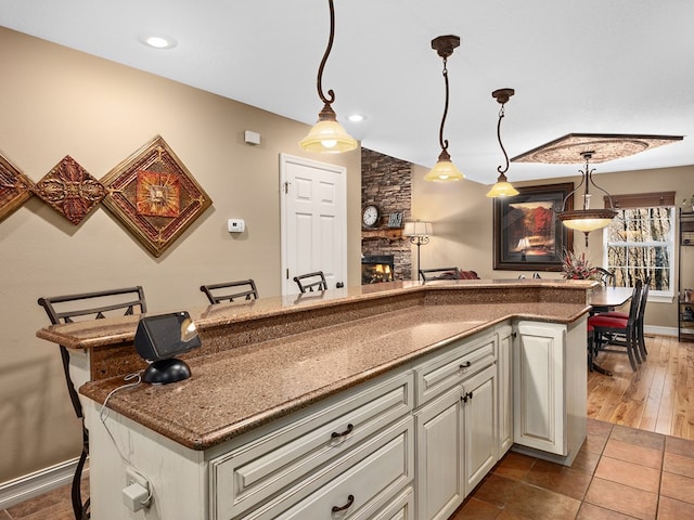 kitchen with a breakfast bar, wood-type flooring, a stone fireplace, hanging light fixtures, and lofted ceiling