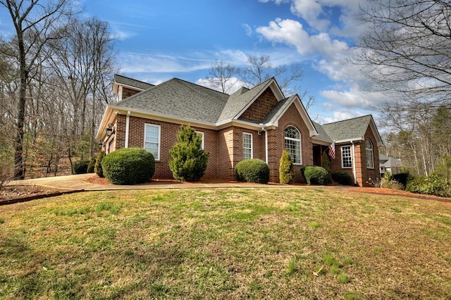 view of front of property featuring brick siding, a front lawn, and roof with shingles