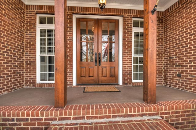 property entrance featuring french doors, a porch, and brick siding