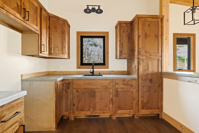 kitchen featuring dark wood-style floors, light countertops, visible vents, brown cabinetry, and a sink