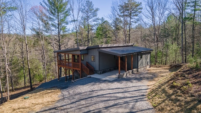 view of front of property with a carport, metal roof, driveway, and a forest view