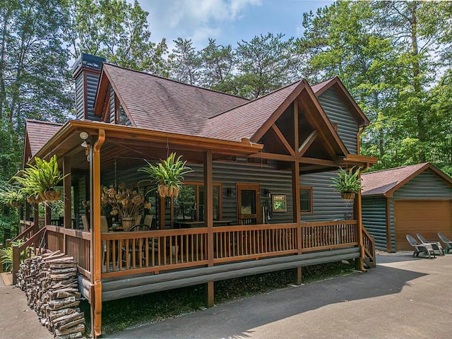 rear view of property with a garage, a porch, and an outbuilding