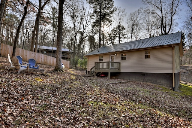 rear view of property featuring a deck, crawl space, fence, and metal roof