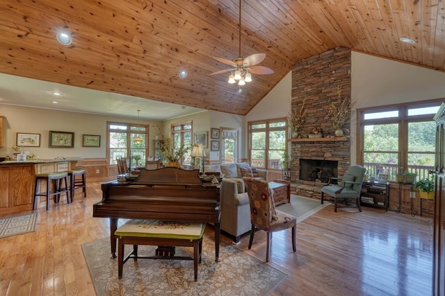 living room with ceiling fan, light wood-type flooring, wood ceiling, a stone fireplace, and high vaulted ceiling