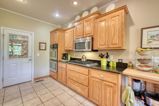 kitchen featuring light tile patterned floors, stainless steel appliances, ornamental molding, and dark stone counters