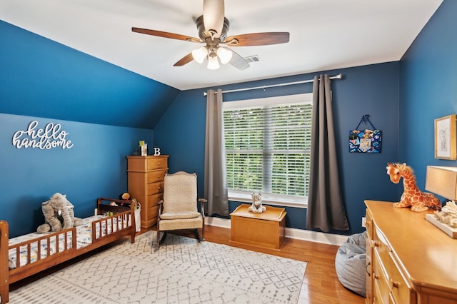 bedroom featuring ceiling fan, lofted ceiling, a nursery area, and light hardwood / wood-style flooring