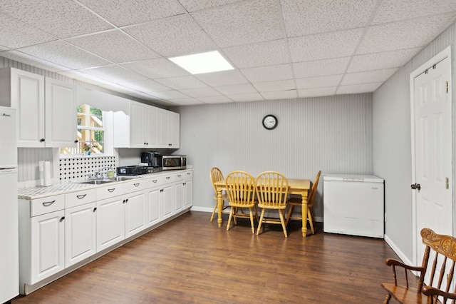 kitchen with a drop ceiling, white cabinetry, dark wood-type flooring, and fridge