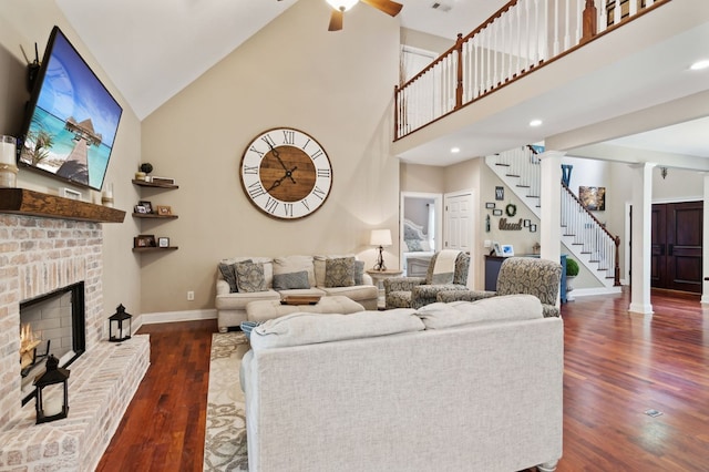 living room featuring dark wood-type flooring, high vaulted ceiling, ceiling fan, ornate columns, and a fireplace