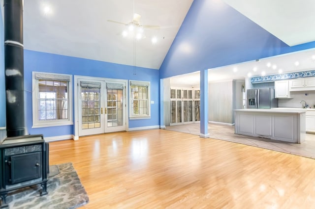 unfurnished living room with light wood-type flooring, high vaulted ceiling, ceiling fan, and a healthy amount of sunlight