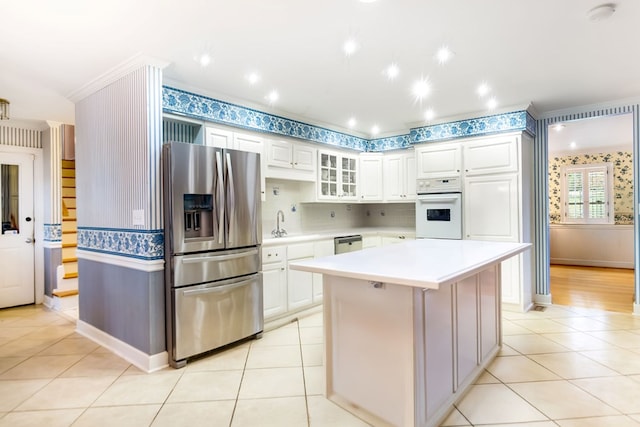 kitchen with a center island, ornamental molding, appliances with stainless steel finishes, light tile patterned flooring, and white cabinetry