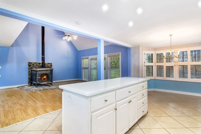 kitchen with a kitchen island, a wood stove, white cabinetry, hanging light fixtures, and light tile patterned flooring