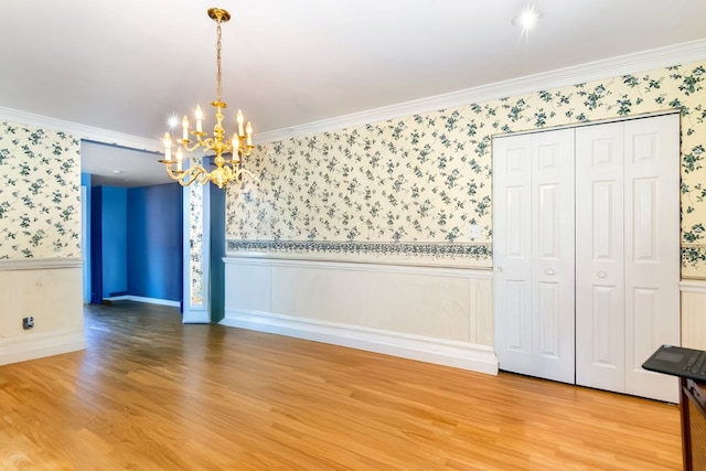 unfurnished dining area featuring wood-type flooring, ornamental molding, and an inviting chandelier