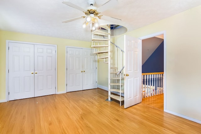 unfurnished bedroom featuring ceiling fan, wood-type flooring, a textured ceiling, and two closets