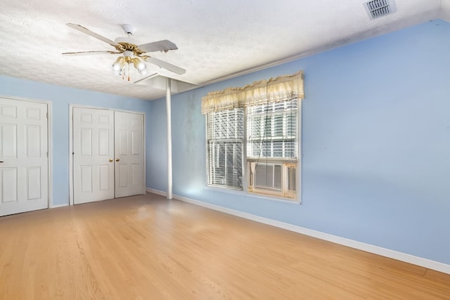 unfurnished bedroom featuring a textured ceiling, light wood-type flooring, ceiling fan, and multiple closets