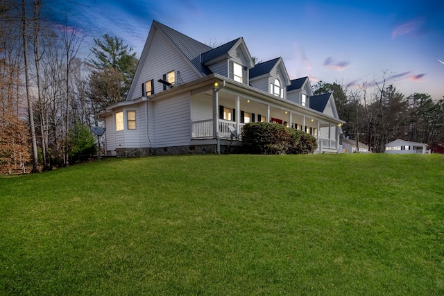 property exterior at dusk with covered porch and a yard