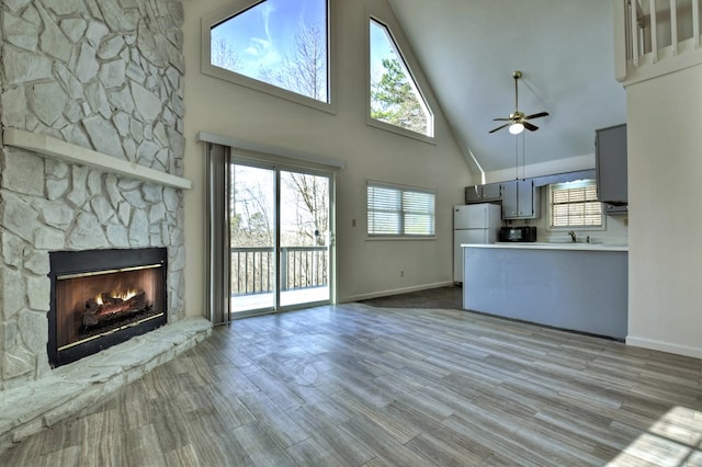 unfurnished living room with a wealth of natural light, a stone fireplace, ceiling fan, and wood finished floors