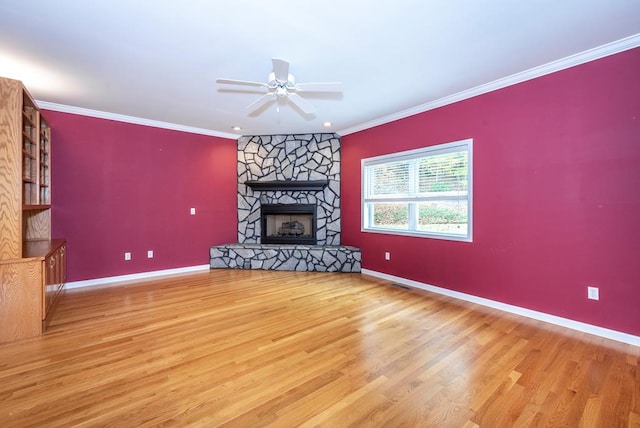 unfurnished living room featuring hardwood / wood-style floors, a stone fireplace, ceiling fan, and ornamental molding